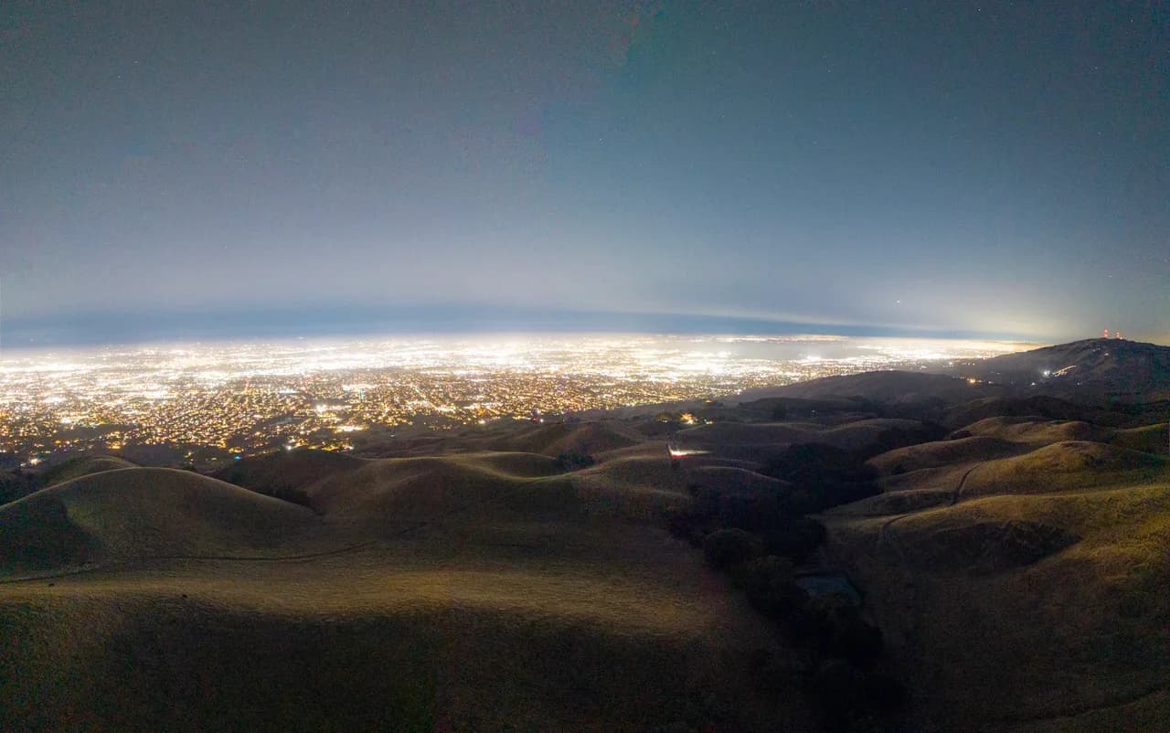 City lights stretch across the horizon beyond dark rolling hills. After Dark photo 1 of 9.