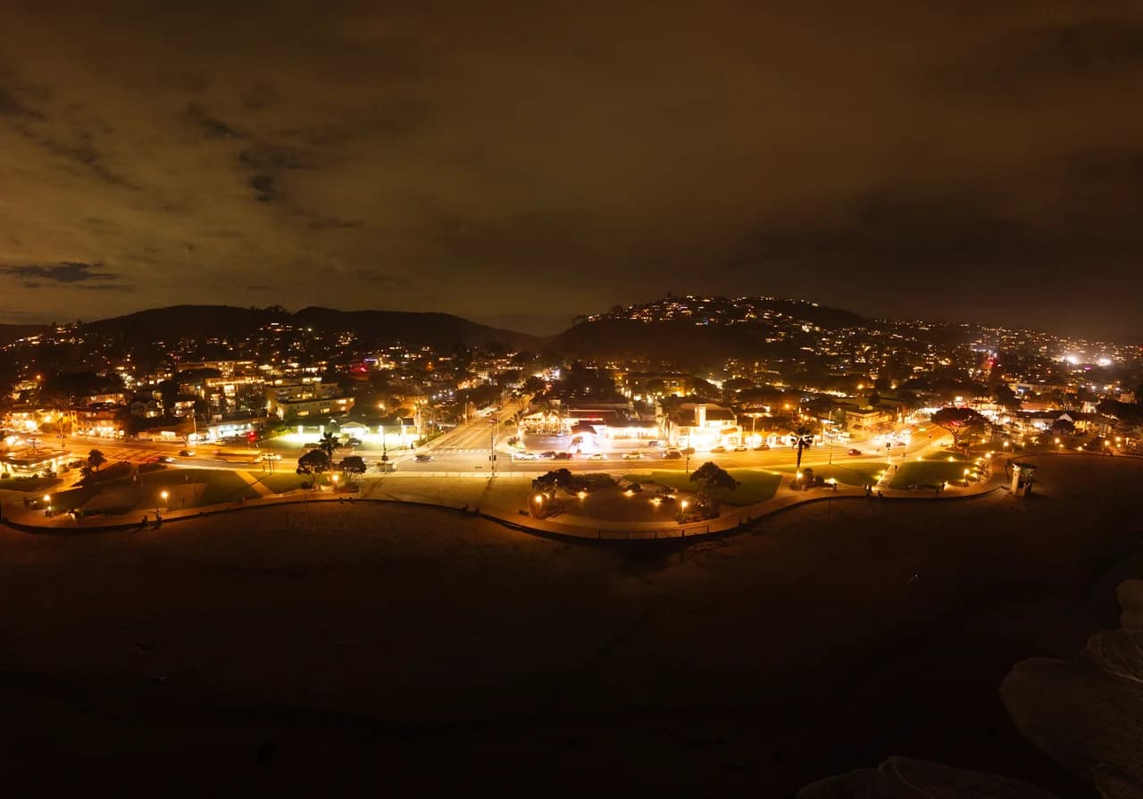 Amber streetlights trace a neighborhood across low hills beneath a cloudy night sky. After Dark photo 9 of 9.