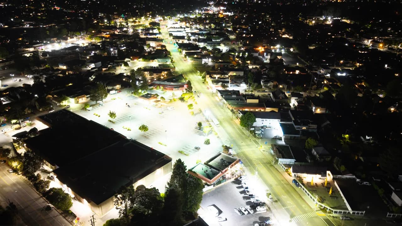 A brightly lit avenue cuts through low buildings and dark residential streets at night. After Dark photo 3 of 9.