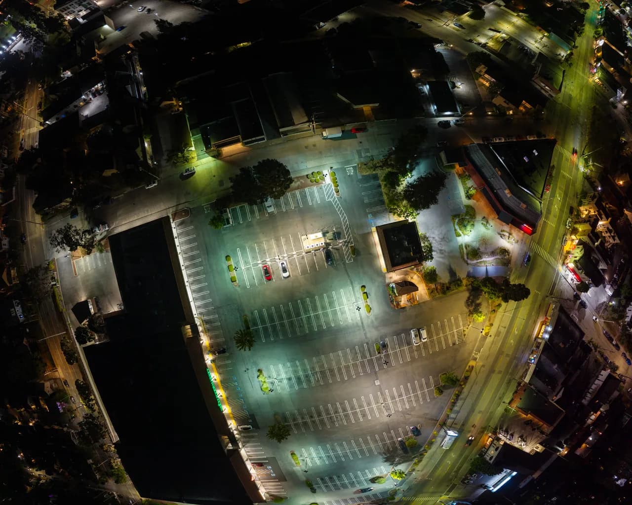 An overhead panorama shows an illuminated parking lot surrounded by dark rooftops and streets. After Dark photo 8 of 9.