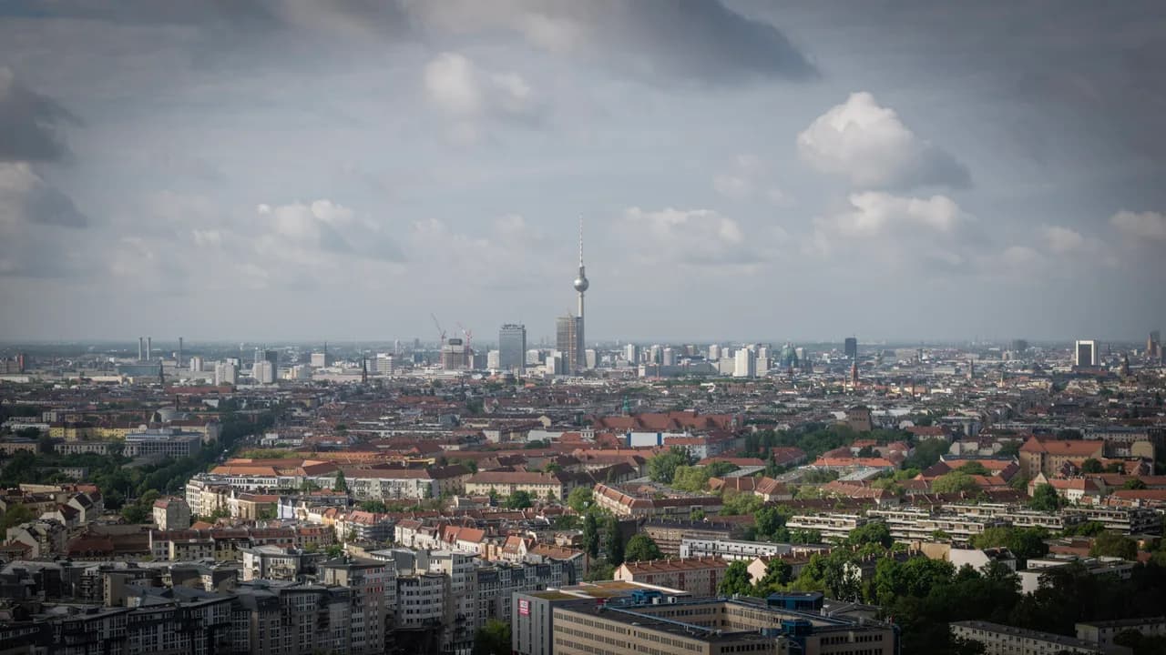 A tall broadcast tower rises above a dense city of pale buildings and red roofs under heavy clouds. Coast & City photo 7 of 11.