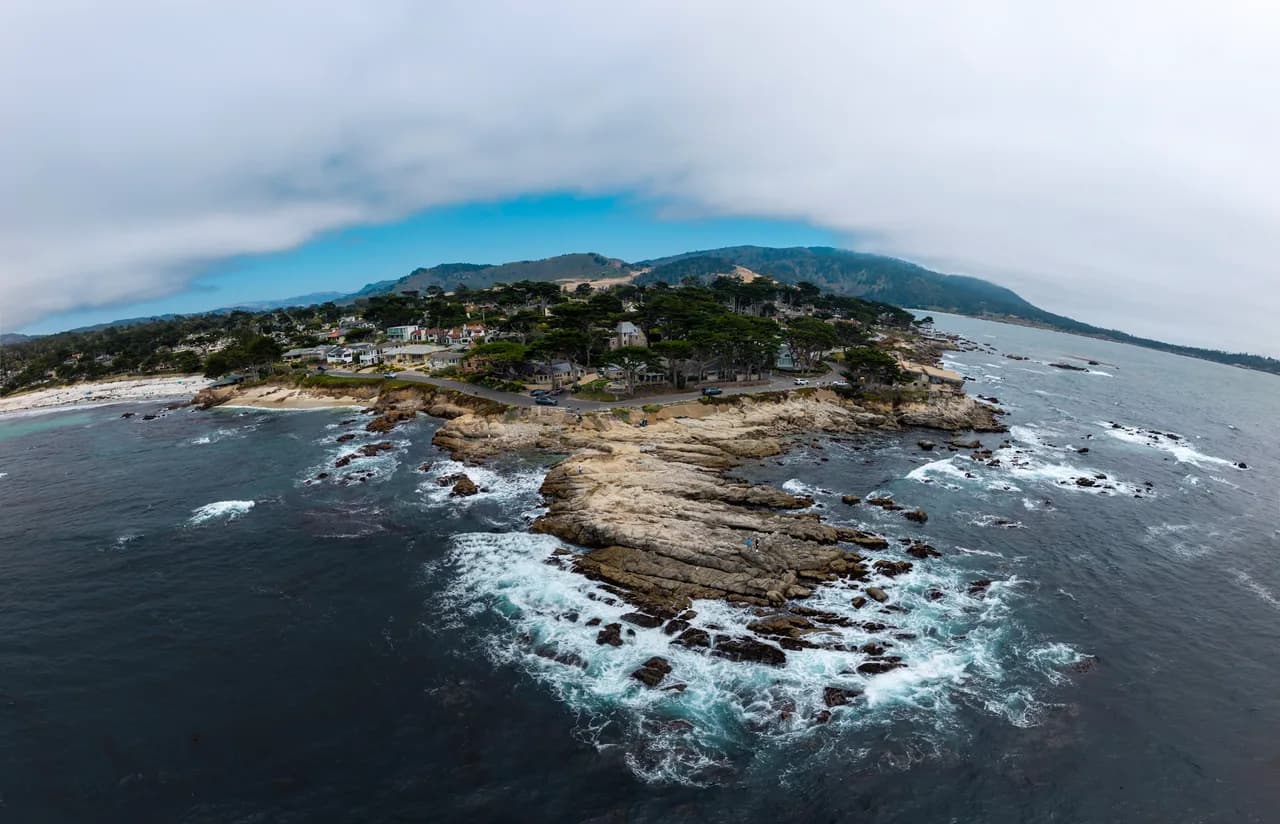 Waves wrap around a rocky headland below a low bank of coastal cloud. Coast & City photo 1 of 11.